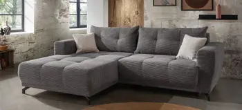 Modernes graues Ecksofa aus Cordstoff mit großzügiger Liegefläche, stilvoll dekoriert mit Kissen, in rustikalem Wohnzimmer mit Betonwand und Holzelementen.